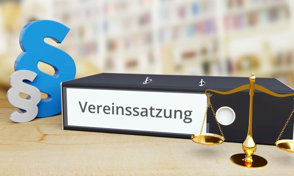 Ordner mit der Beschriftung „Vereinssatzung“ und daneben stehen zwei Paragraphenzeichen und eine Waage.