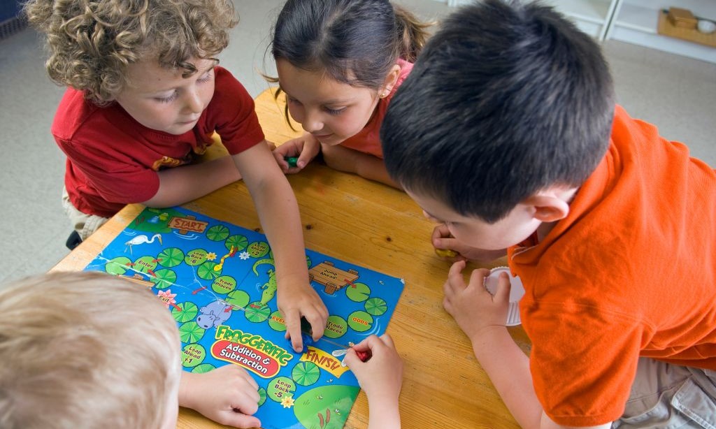 Vier kleine Kinder spielen ein Gesellschaftsspiel. 