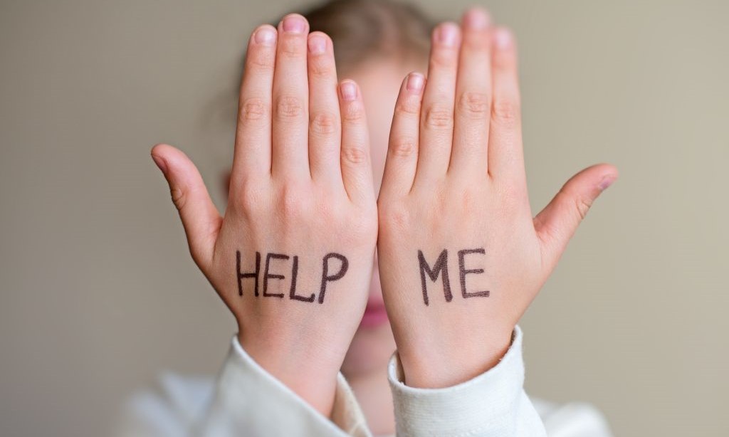 Ein Mädchen hält sich beide Hände vor das Gesicht und auf den Händen steht „Help me“.