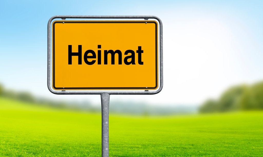 Ein Straßenschild mit dem Begriff „Heimat“ steht vor einem unscharfen Hintergrund.