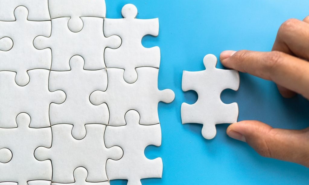 Hand legt weiße Puzzlestücke auf blauen Hintergrund