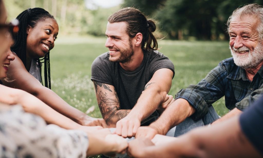 Menschen sitzen im Park zusammen und halten ihre Fäuste in die Mitte.