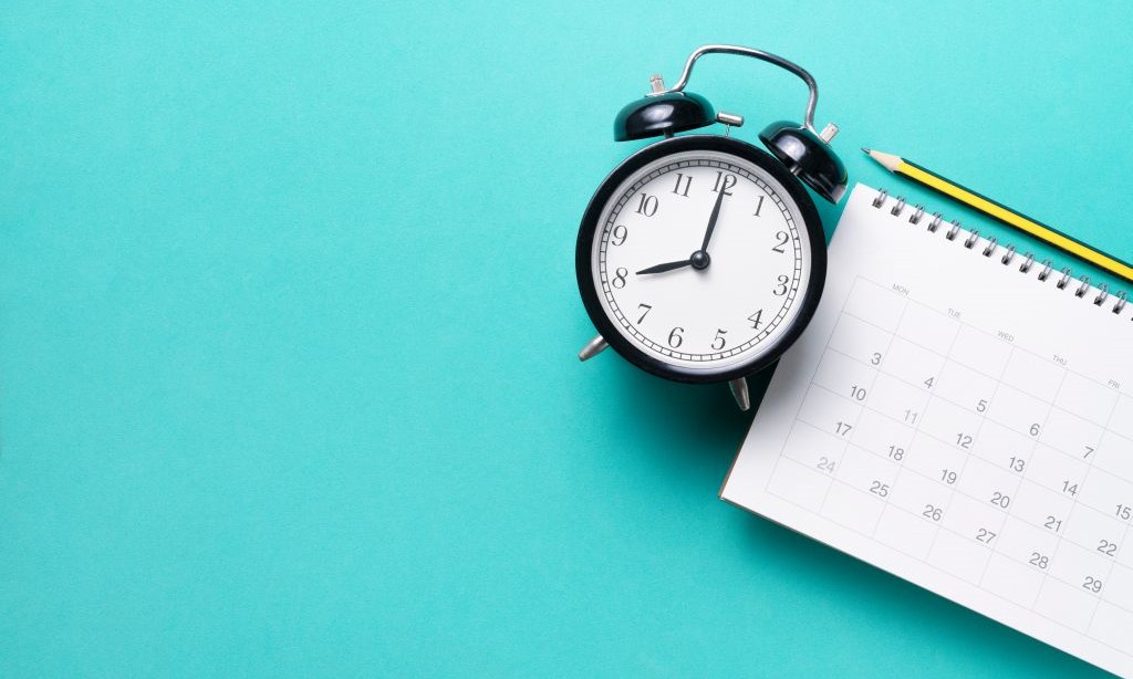 Wecker und Kalender liegen auf blauem Untergrund