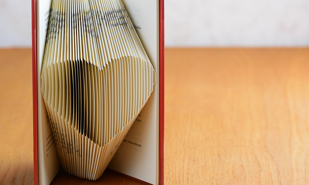 Aufgestelltes Buch mit rotem Einband, dessen Seiten so gefaltet und aufgefächert sind, dass sie ein Herzrelief bilden. 