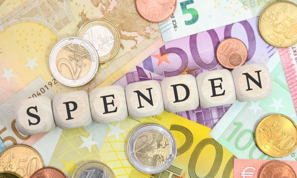Holzwürfel mit Buchstaben bilden das Wort „Spenden“ und liegen auf Euroscheinen. 