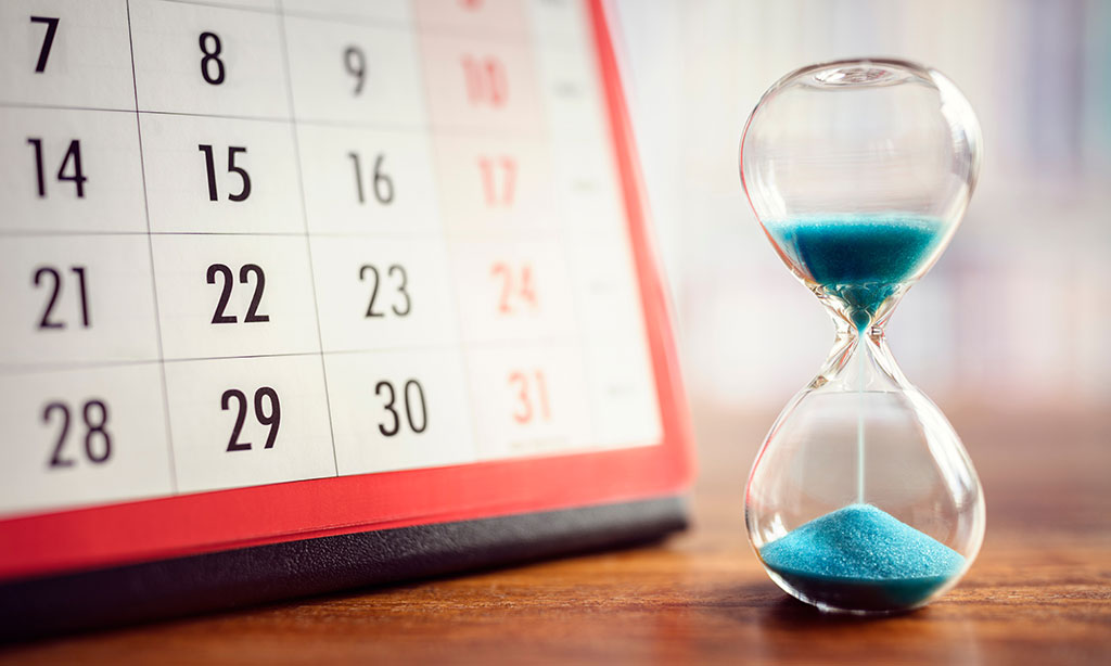 Auf einem Tisch stehen ein Kalender und eine Sanduhr. 