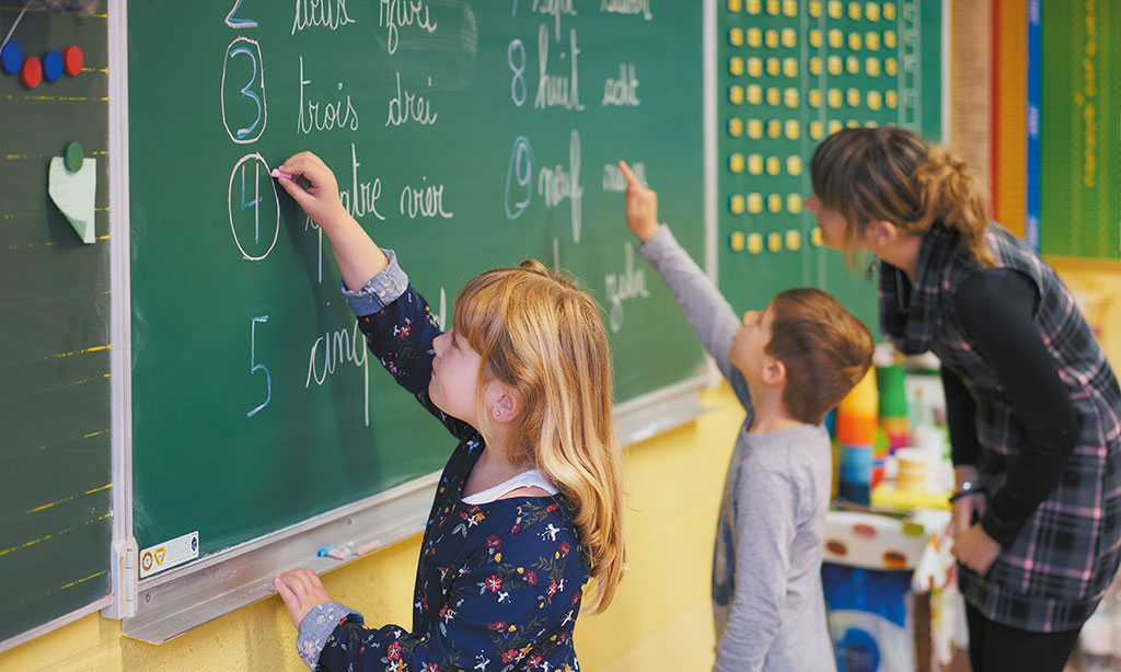 Zwei Schulkinder schreiben mit Kreide etwas an die Tafel.