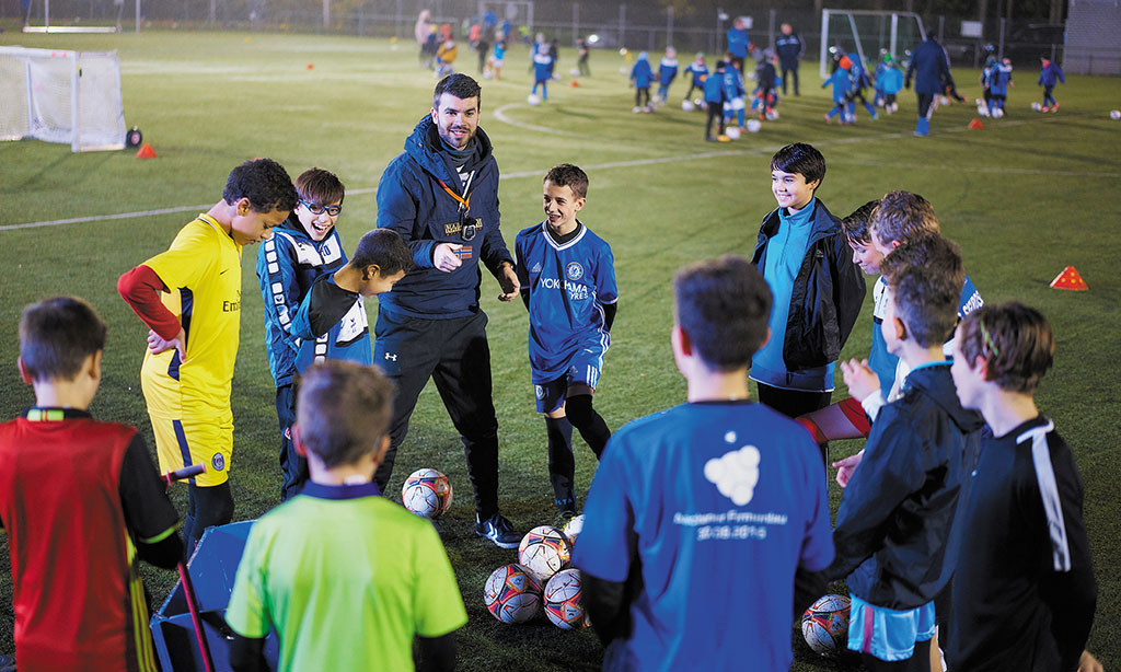 Ein junger Mann animiert Kinder bei einer Fußball-Aktivität.