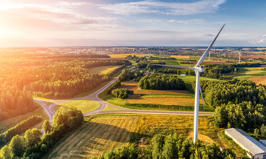 Eine Straße mit Kreisverkehr in der Natur und ein Windrad auf dem Feld.