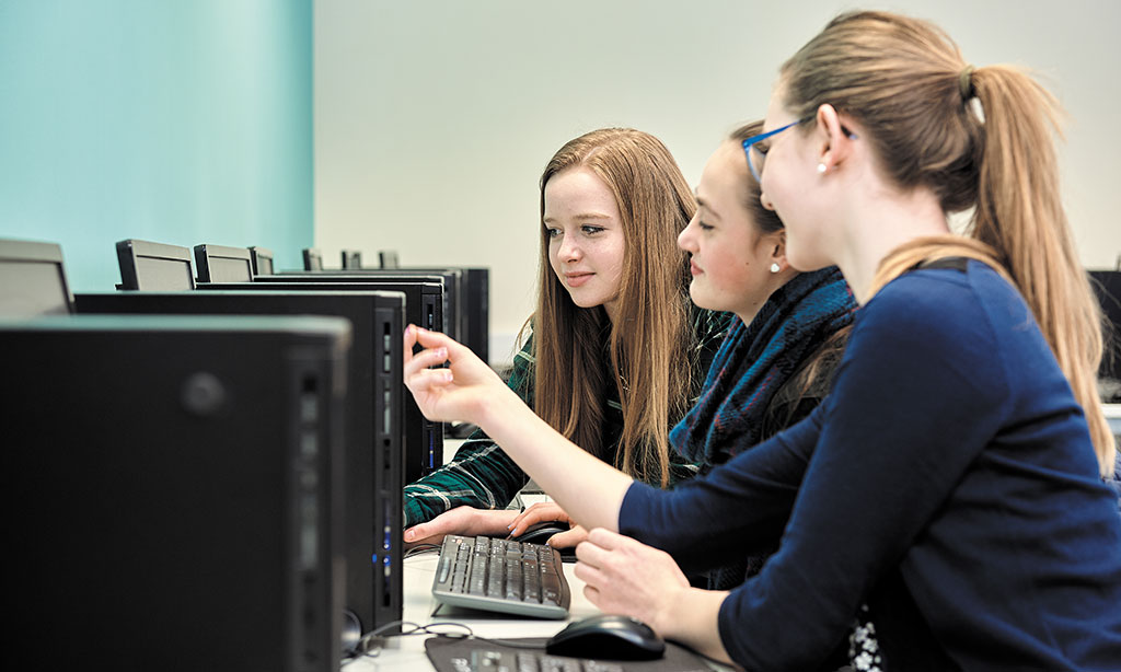 Drei Jugendliche sitzen an einem Computer.