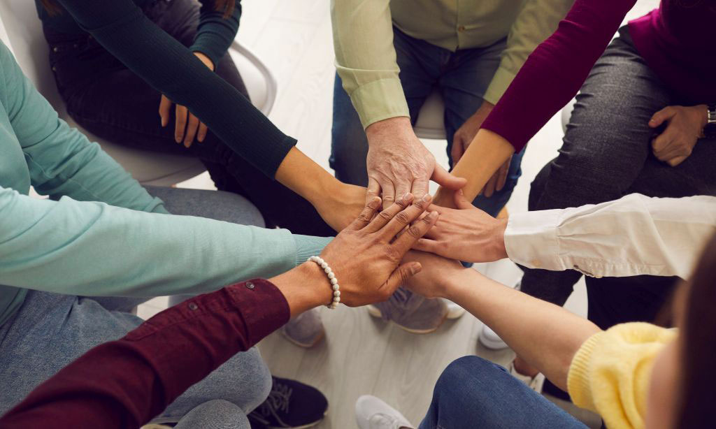 Verschiedene Menschen legen ihre Hände in der Mitte übereinander.