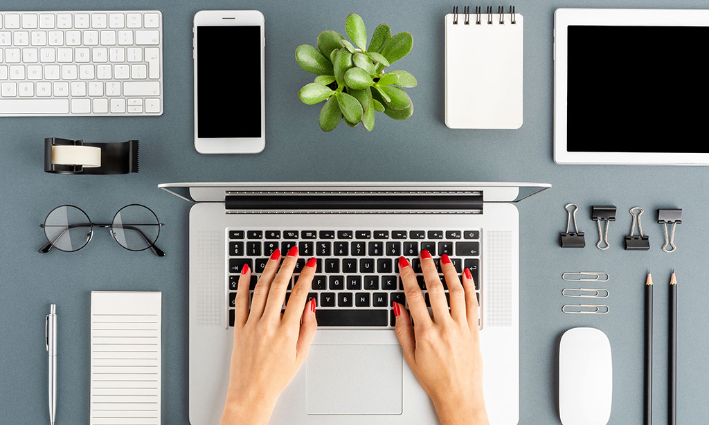 Frau arbeitet an Laptop, neben dem Smartphones und diverses Büromaterial liegt