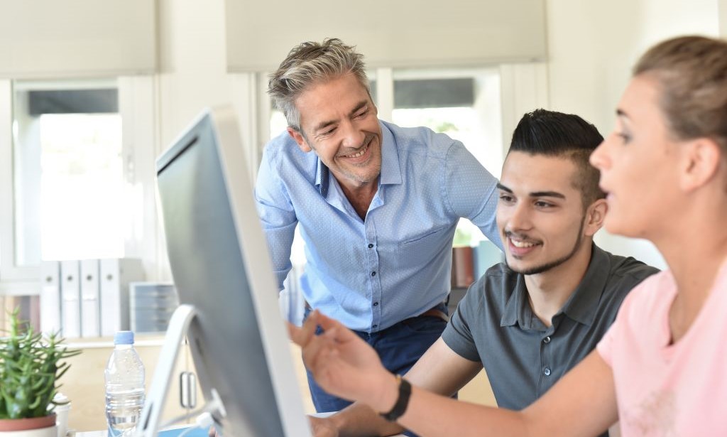 Ein Mann und eine Frau zeigen einem Studenten etwas am Computer.