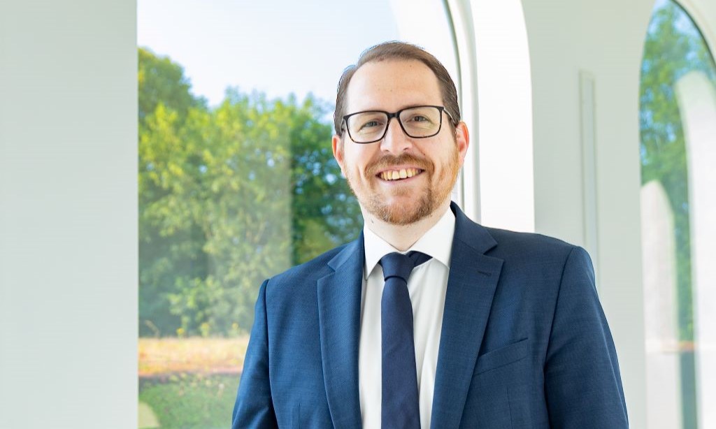 Portrait Jérôme Franssen vor einem Fenster mit Blick auf grüne Bäume