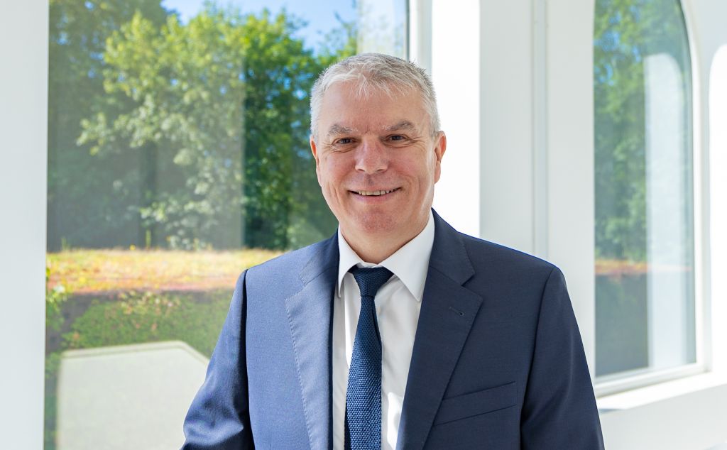 Portrait Gregor Freches vor einem Fenster mit Blick auf grüne Bäume