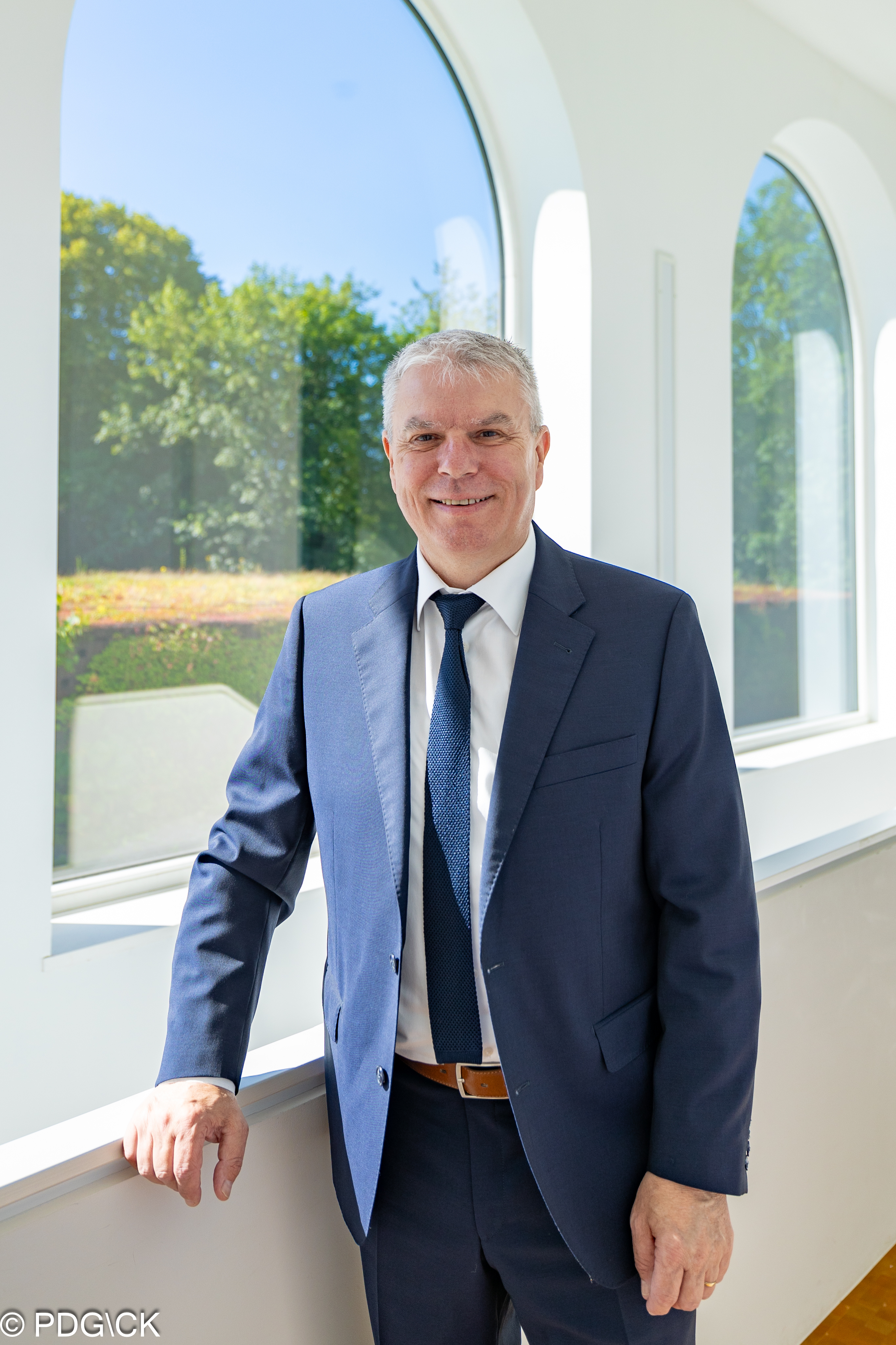 Portrait Gregor Freches vor einem Fenster mit Blick auf grüne Bäume