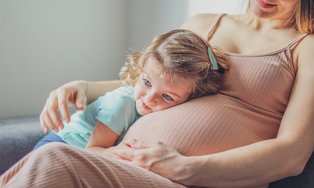 Kleinkind schmiegt sich an den Babybauch seiner Mutter