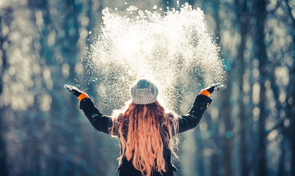 Junge Frau schmeißt Schnee in die Luft