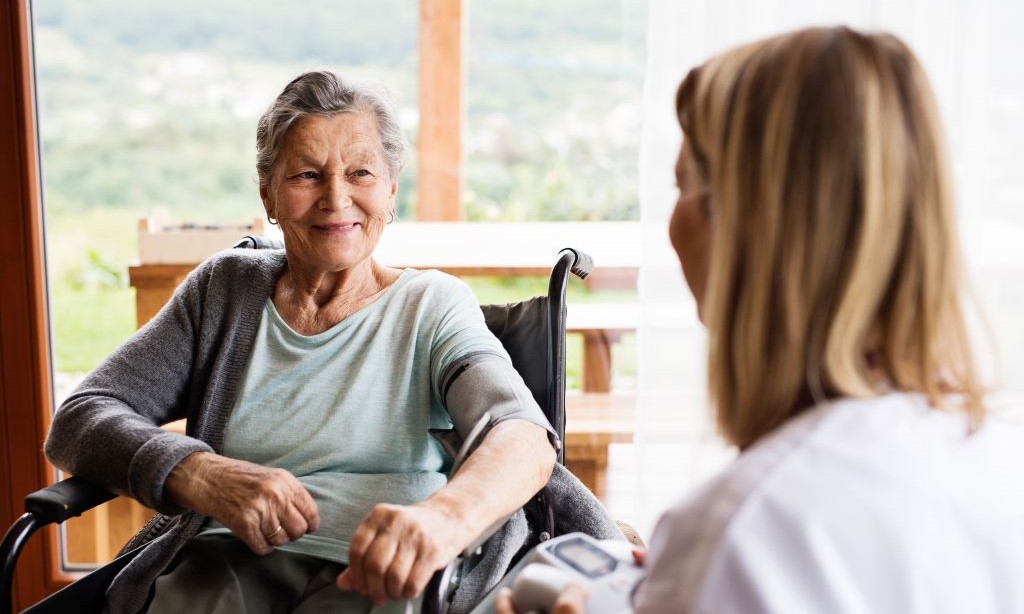 Eine Pflegerin misst einer Seniorin im Rollstuhl den Blutdruck.