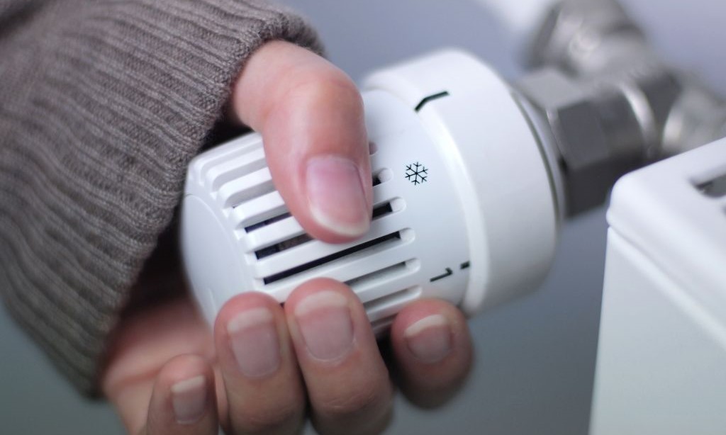 Ein Person dreht am Thermostat einer Heizung.
