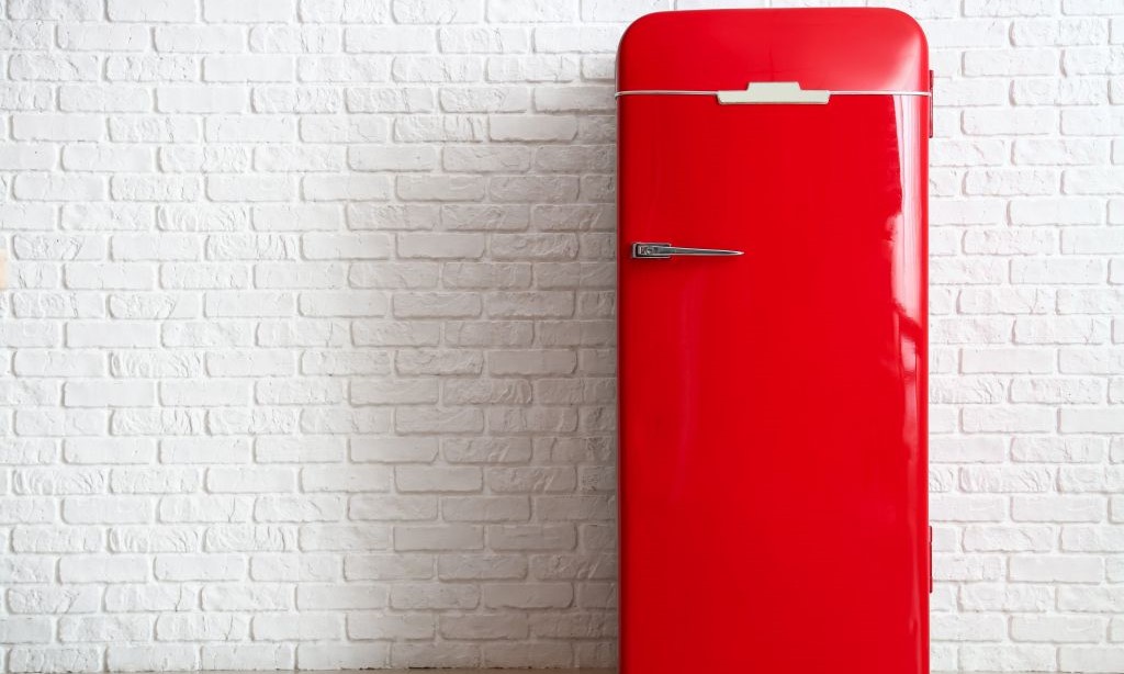 Ein roter Kühlschrank steht von einer weißen Ziegelwand.