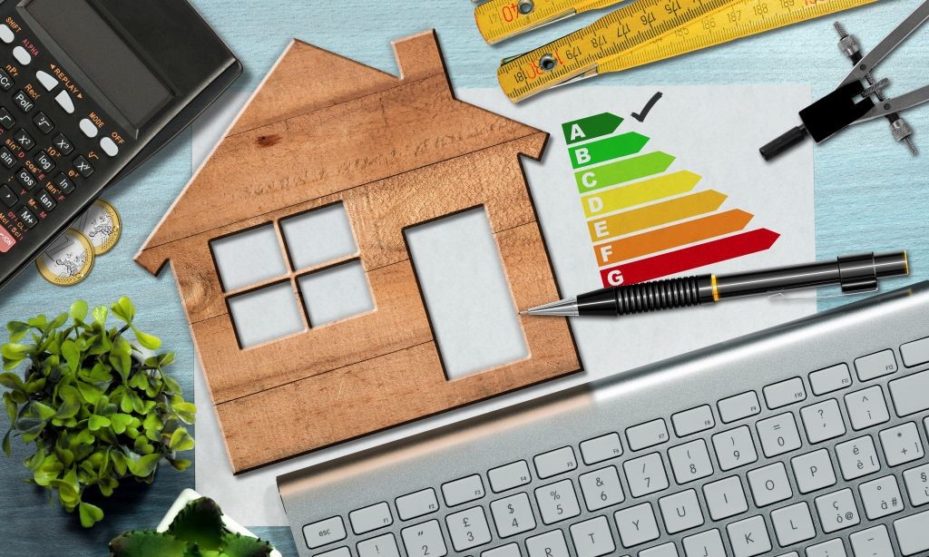 Über einer Tastatur liegt das Modell eines Hauses aus Holz. Daneben liegt die Abbildung des Energielabels.