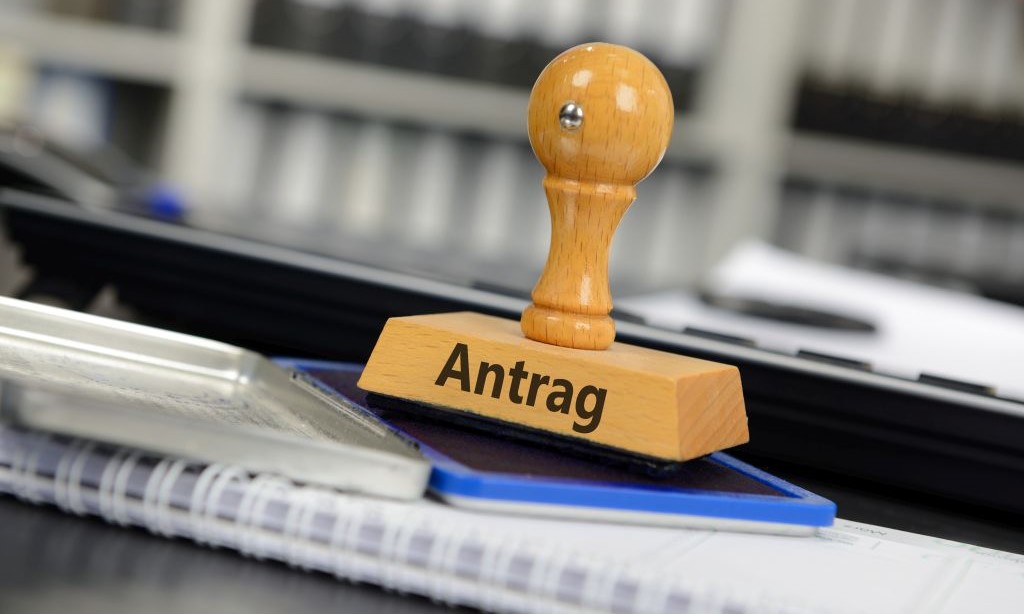 Ein Stempel mit der Aufschrift Antrag steht auf einem Notizblock.