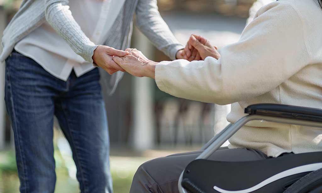 Eine Frau hält die Hände einer anderen Frau, die im Rollstuhl sitzt