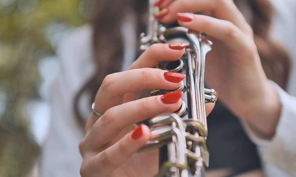 Eine Frau mit rot lackierten Fingernägeln spielt Klarinette.