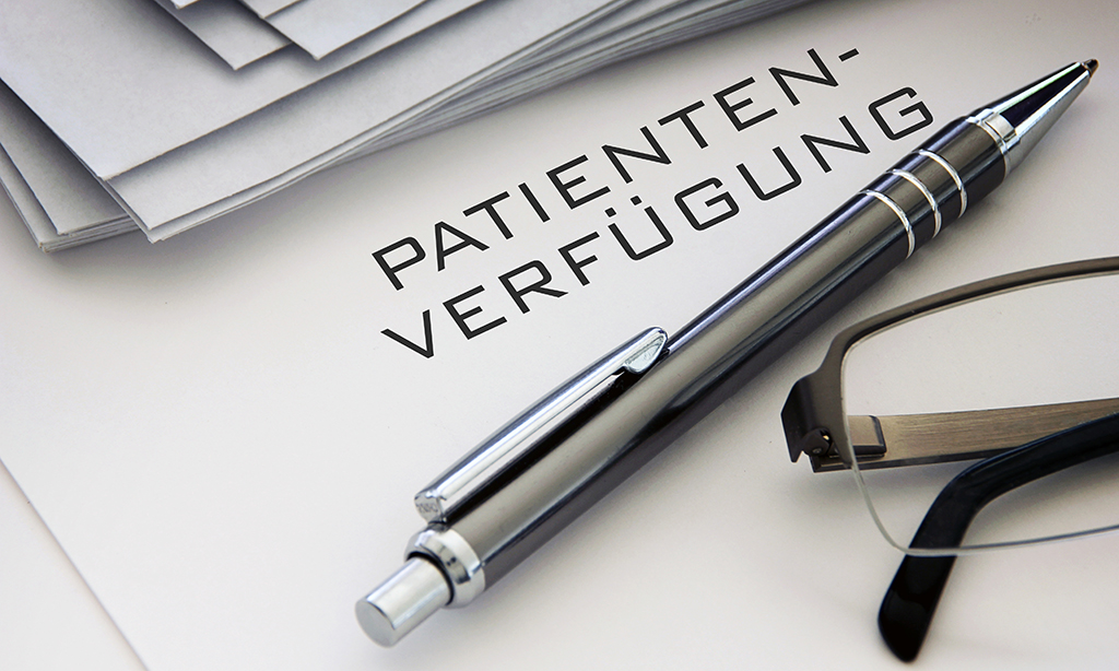 Auf einem Tisch liegt ein Papier mit der Aufschrift Patientenverfügung neben einem Kugelschreiber und einer Brille.
