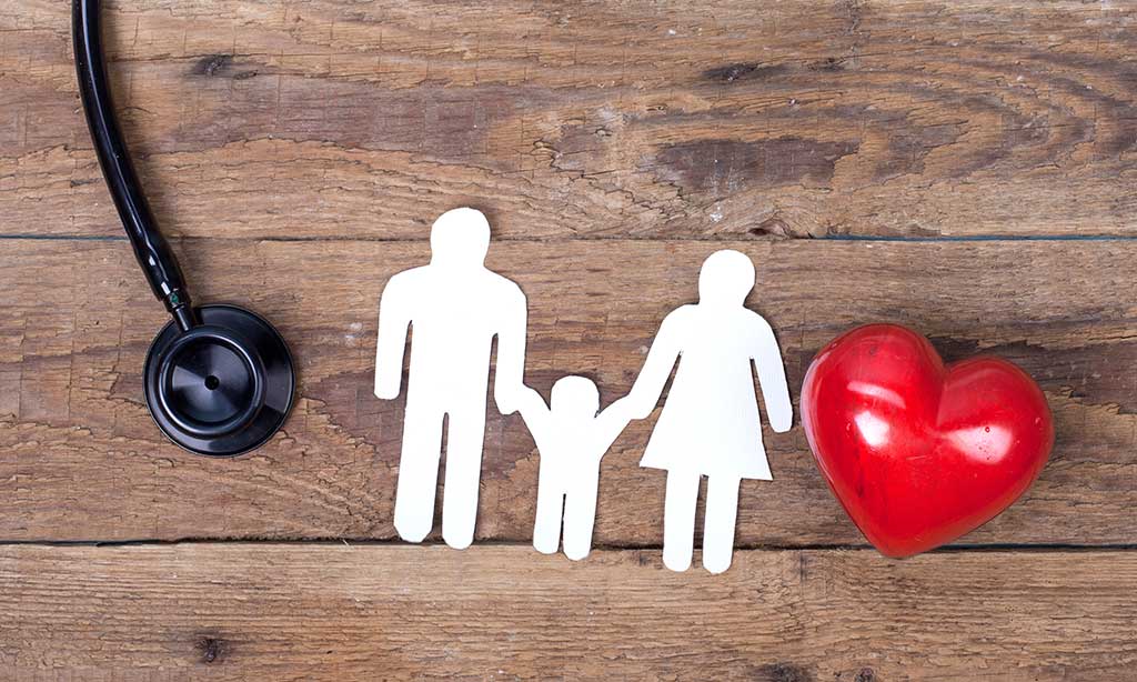 Zwischen einem Stethoskop und einem Herzen ist eine aus Papier ausgeschnittene Familie.