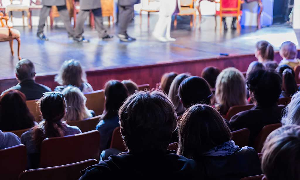 Menschen sitzen in einem Theater und schauen sich eine Aufführung an.
