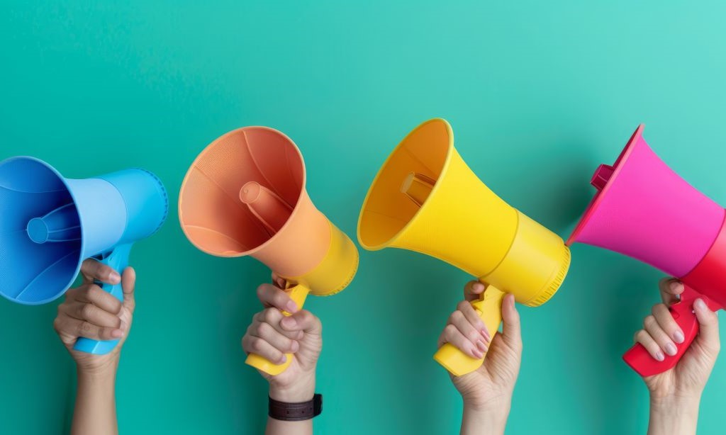Vier Hände halten bunte Megaphone vor einen grünen Hintergrund.