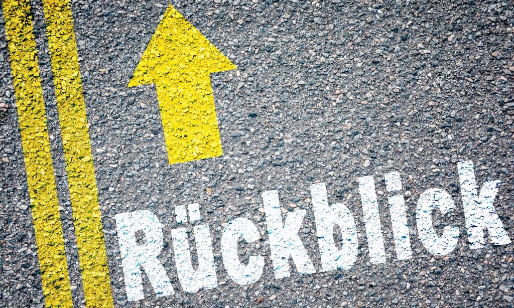 Auf einer Straße ist in gelber Farbe Rückblick geschrieben und darüber ist ein gelber Pfeil.