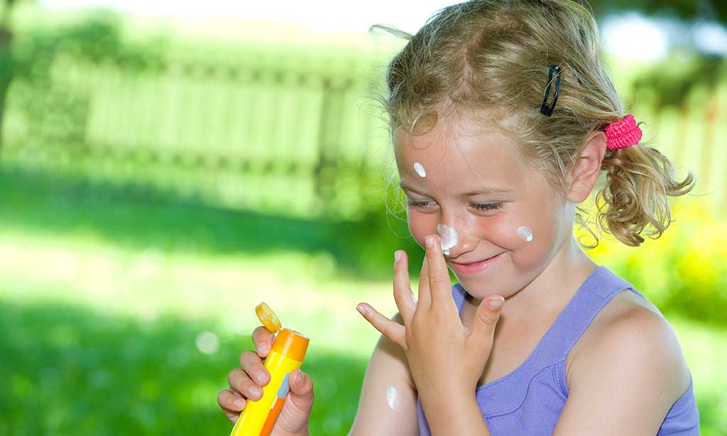 Ein Kind reibt sich mit Sonnencreme ein.