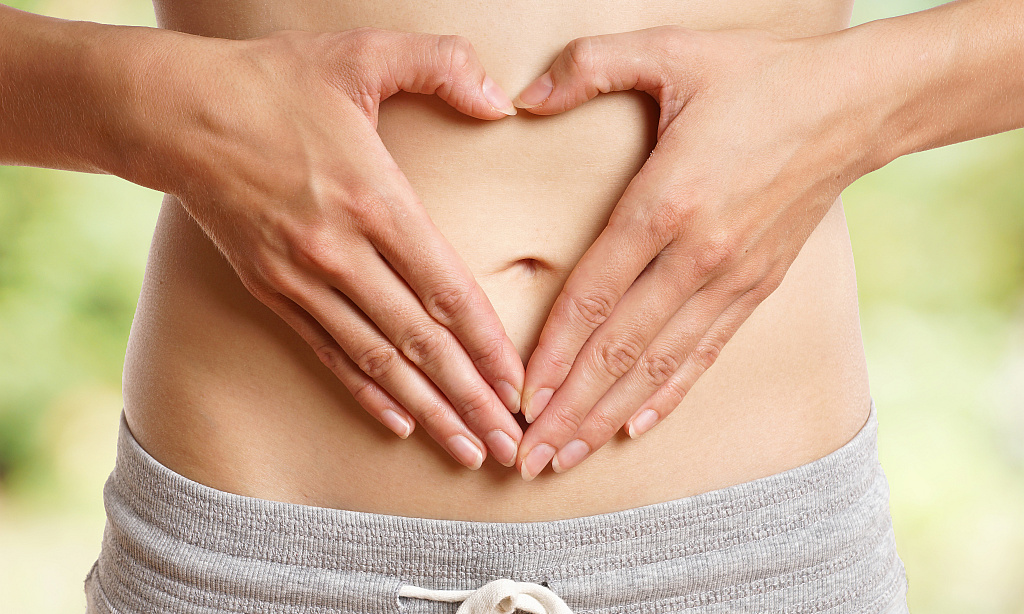 Frau formt vor ihrem Bauch ein Herz mit ihren Herzen.