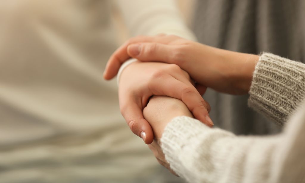 Eine Person hält mit beiden Händen die Hand einer zweiten Person.
