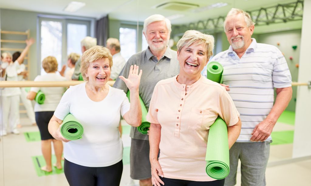 Vier alte Menschen haben Yoga-Matten in der der Hand und lächeln in die Kamera.