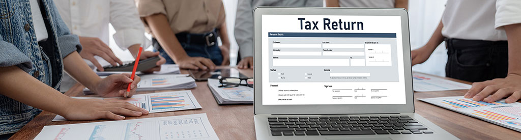 Mehrere Personen stehen um einen Tisch mit einem Bildschirm, auf dem das Wort Tax Return steht.